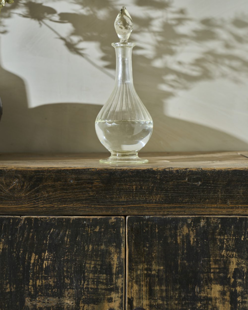 Carafe en verre, ombres végétales et meuble en bois ancien
